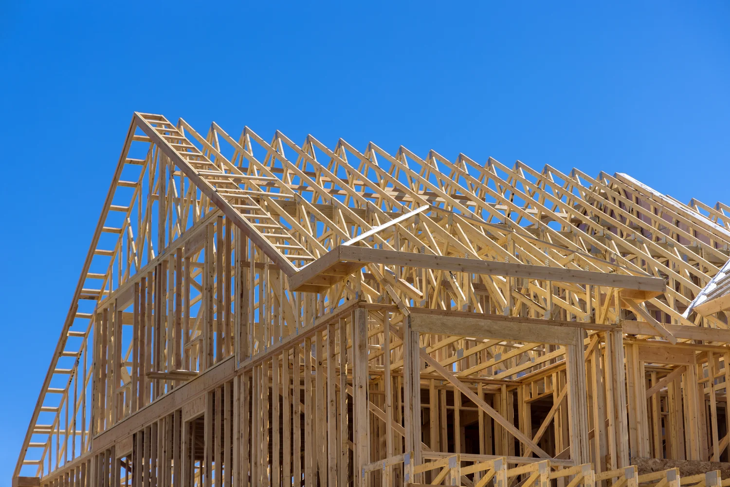 Wooden framework of a house under construction against a clear blue sky.