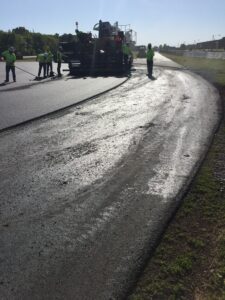 Workers paving a road with fresh asphalt on a sunny day.
