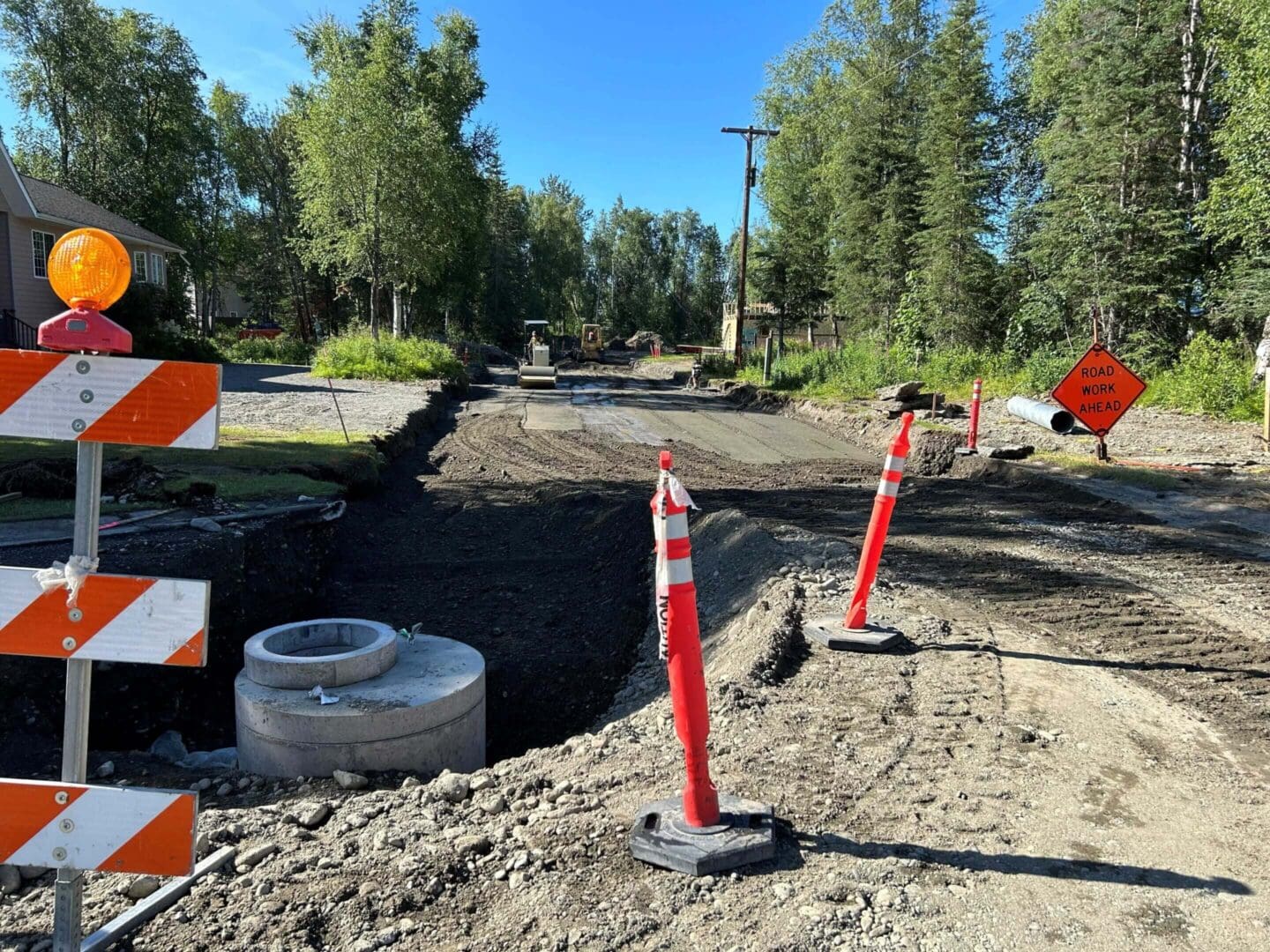 Road construction site with trees and safety cones.