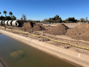 A canal next to a construction site with piles of dirt and large pipes.