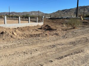 A dirt road near a partially constructed fence in a desert landscape.