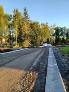 A newly paved road with trees and houses alongside it.