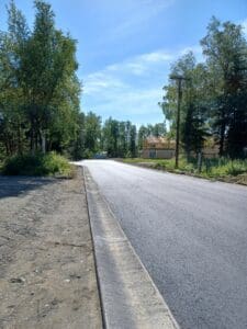 A newly paved road surrounded by trees and a clear blue sky.
