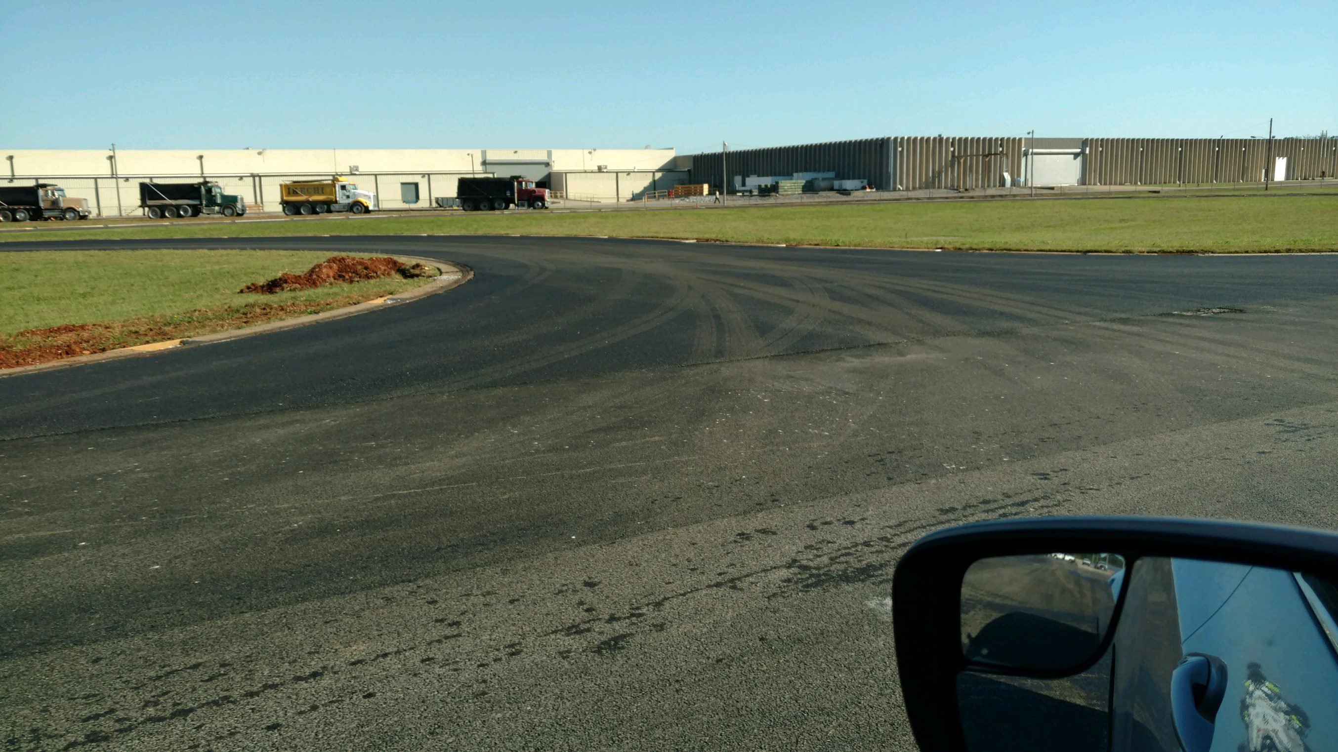 SUMITOMO 3 Wide paved road curving near industrial buildings under a clear sky.