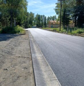 A newly paved road surrounded by trees and a clear sky.