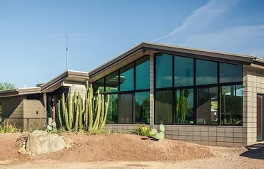 Modern house with large glass windows and cacti outside.