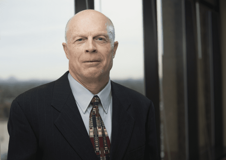 A bald man in a suit and tie standing indoors.