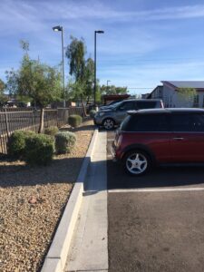 A parking lot with a red car and a black SUV under a clear sky.