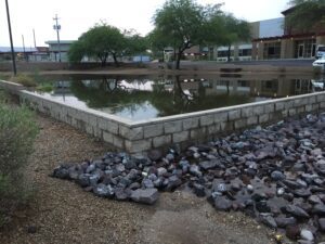 A small rectangular pond surrounded by gravel and rocks with trees in the background.
