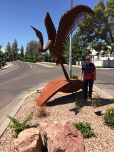 A large metal bird sculpture near a curved road with a person standing beside it.