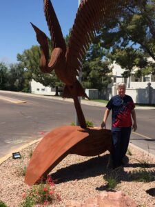 Person posing next to large metal leaf sculpture outdoors.